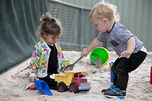 A girl and boy toddler playing in the sand pit together