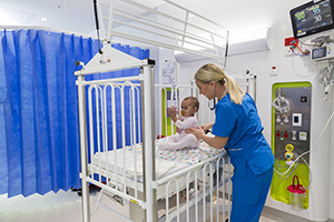 Nurse holding baby sitting in cot