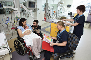 Mum in wheelchair holding baby with KEMH staff and dad