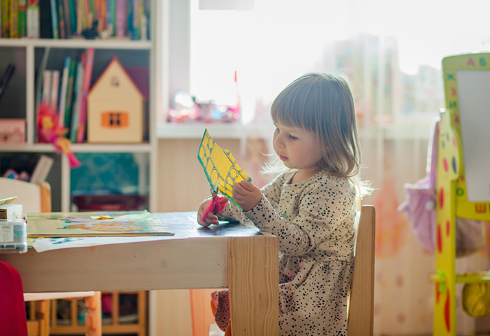 Little girl cutting out a sheet sitting in a playroom