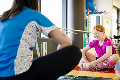 Girl sitting on floor with legs crossed, smiling at her physiotherapist