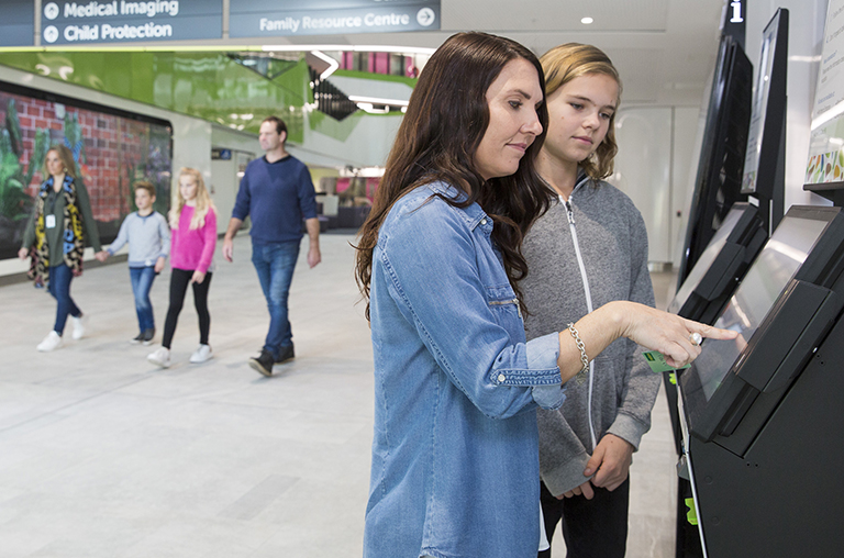 Mother and son use self check-in kiosk in PCH Atrium